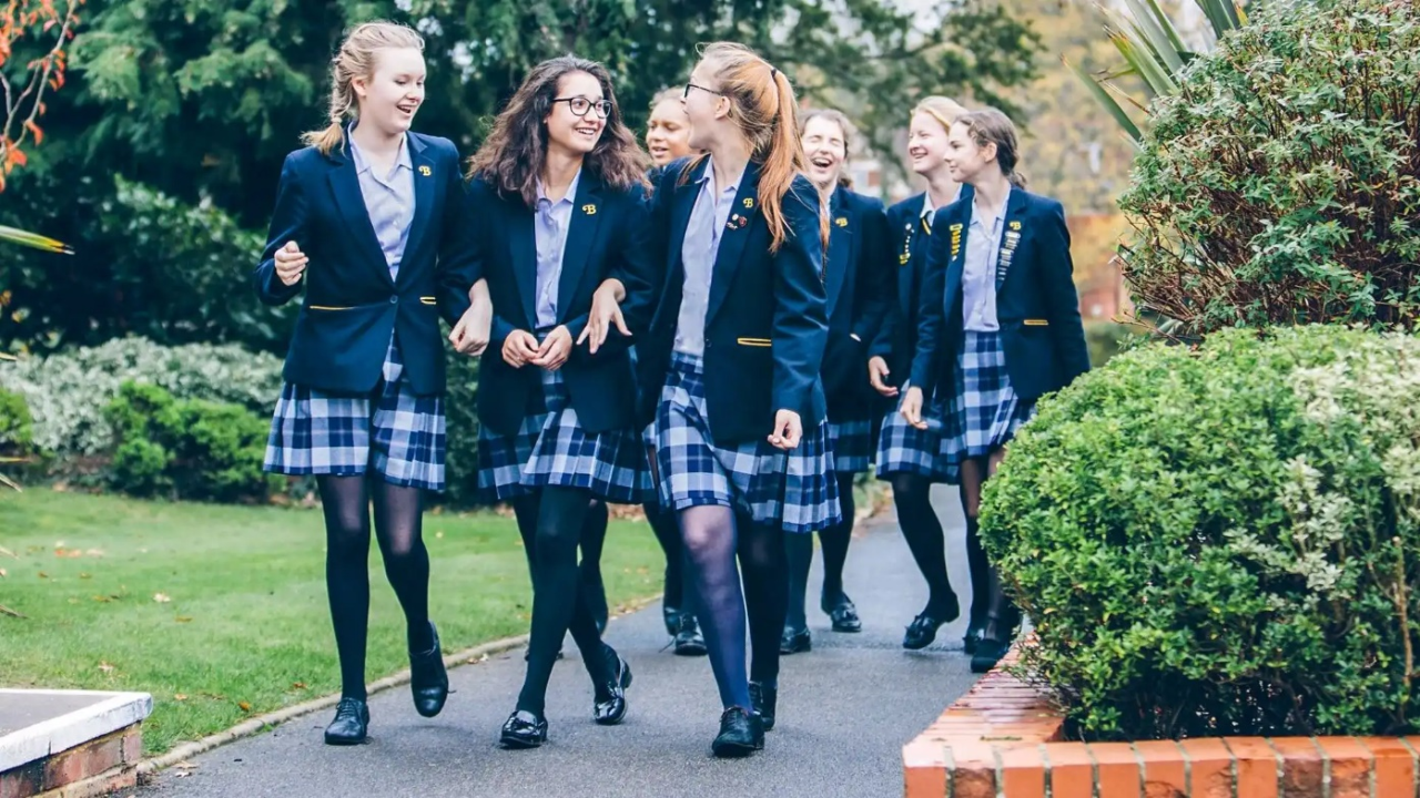 A group of girls in school uniforms walking on a sidewalk

Description automatically generated